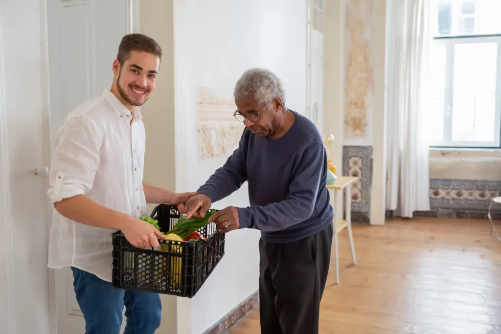 Volunteer delivering a crate of fresh food to an older man at home